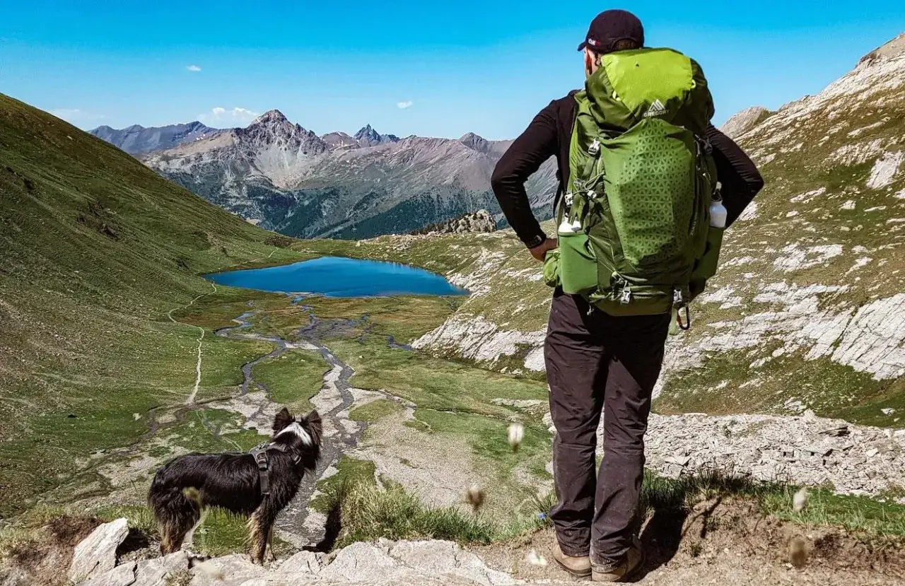 Un randonneur et son chien contemplent un lac bleu et des montagnes majestueuses. Une belle journée pour randonner avec son chien.
