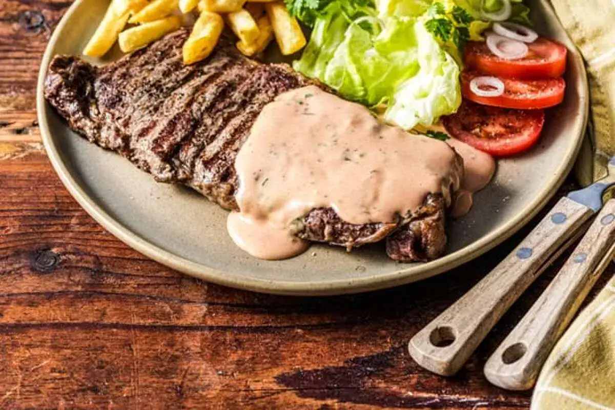 Entrecôte grillée généreusement nappée d'une sauce onctueuse, accompagnée de frites croustillantes, d'une salade fraîche et de tomates. Un délice pour les amateurs de sauce pour entrecôte au barbecue.