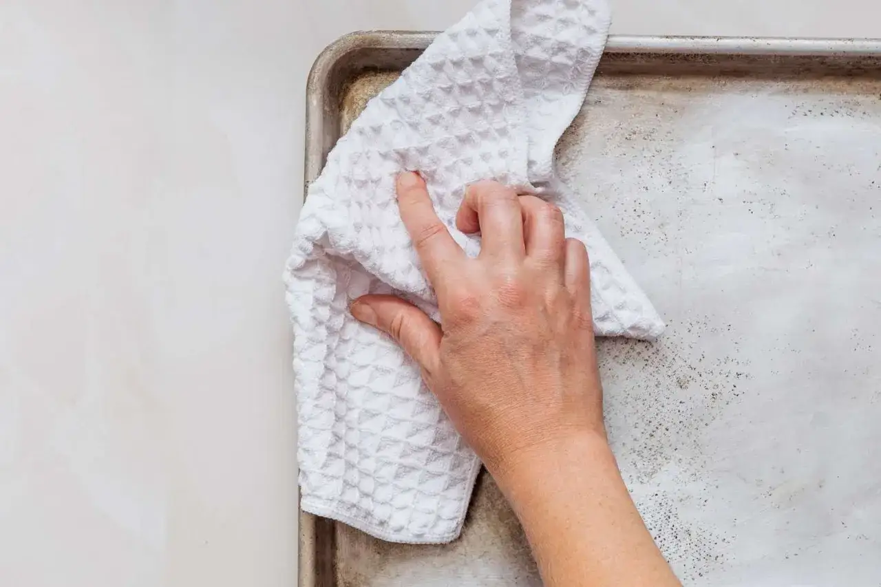 Mano limpiando una bandeja de aluminio con un paño blanco. Un ejemplo de como limpiar el aluminio para que quede reluciente.