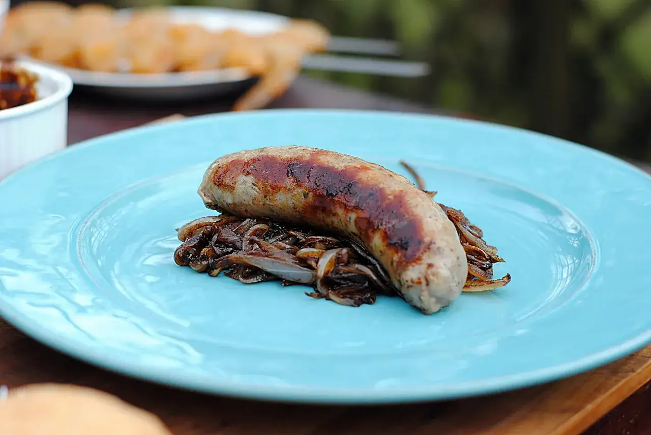 Grillowana kiełbasa z karmelizowaną cebulką na turkusowym talerzu. Pyszne danie, które z pewnością dostarczy wielu wrażeń smakowych, a jego kiełbasa z grilla kcal jest idealna na letnie wieczory.