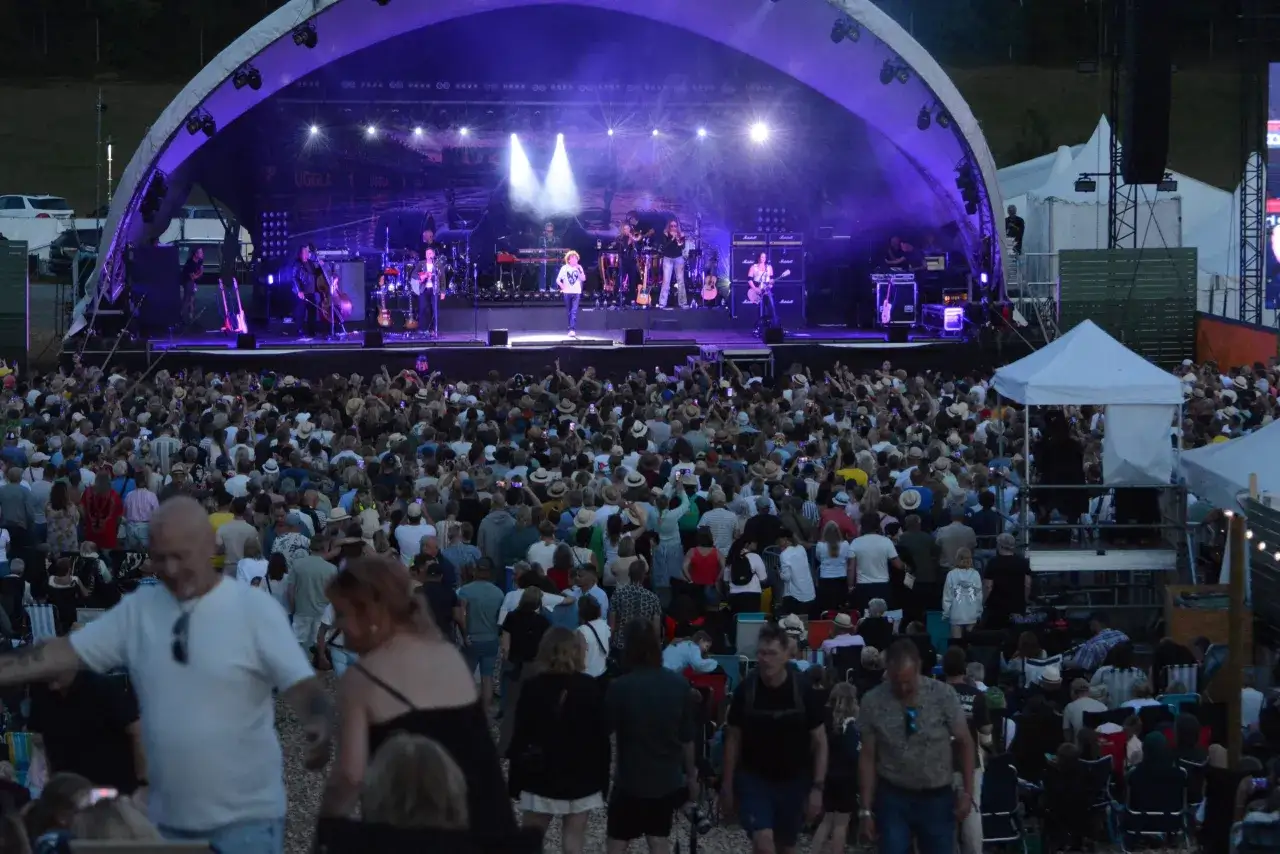 Stor publik njuter av en konsert under ett kultur festival. Bandet spelar på en upplyst scen med lila ljus.
