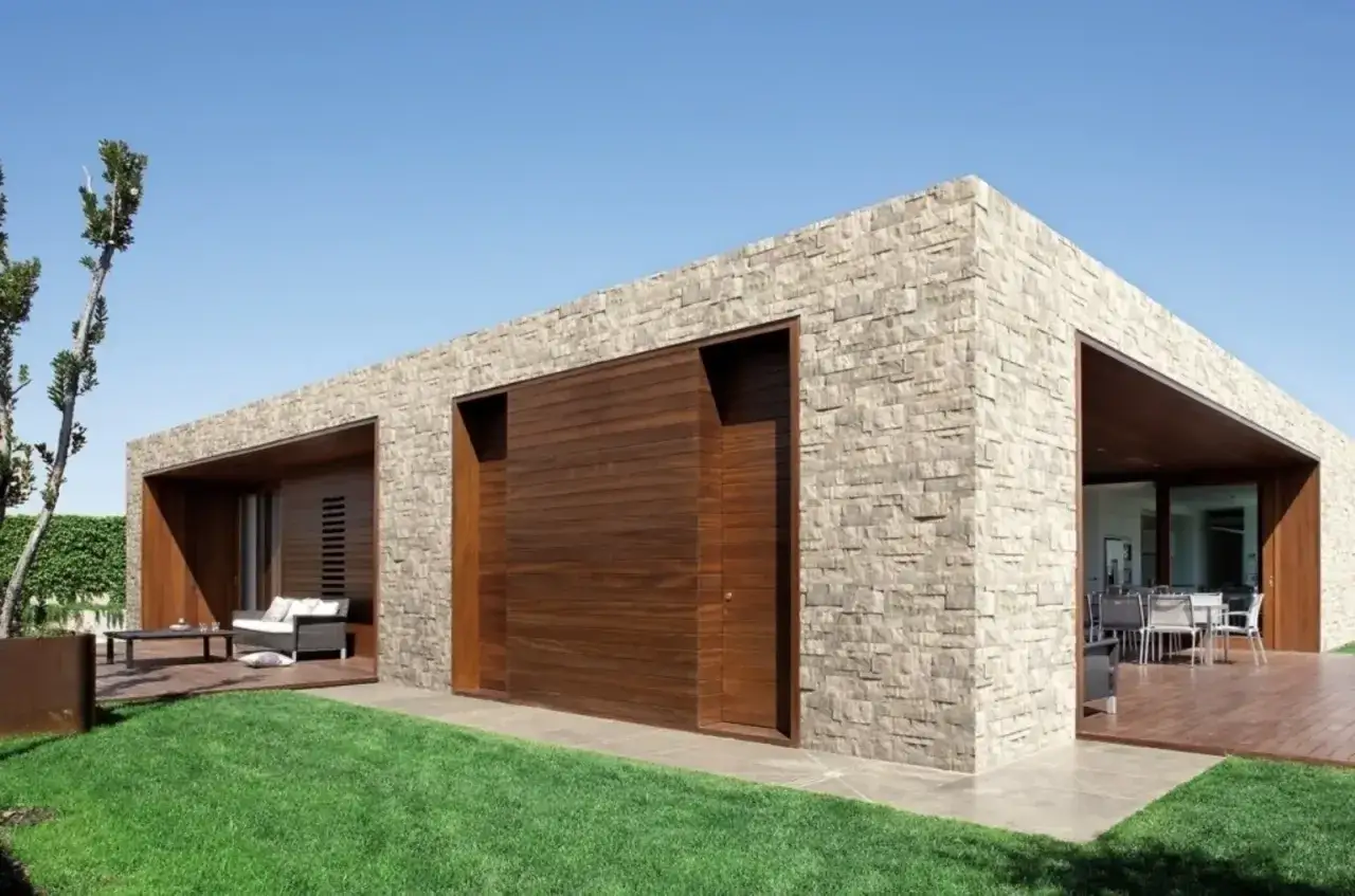 Moderna villa con eleganti facciate in pietra, ampie vetrate e un patio in legno.