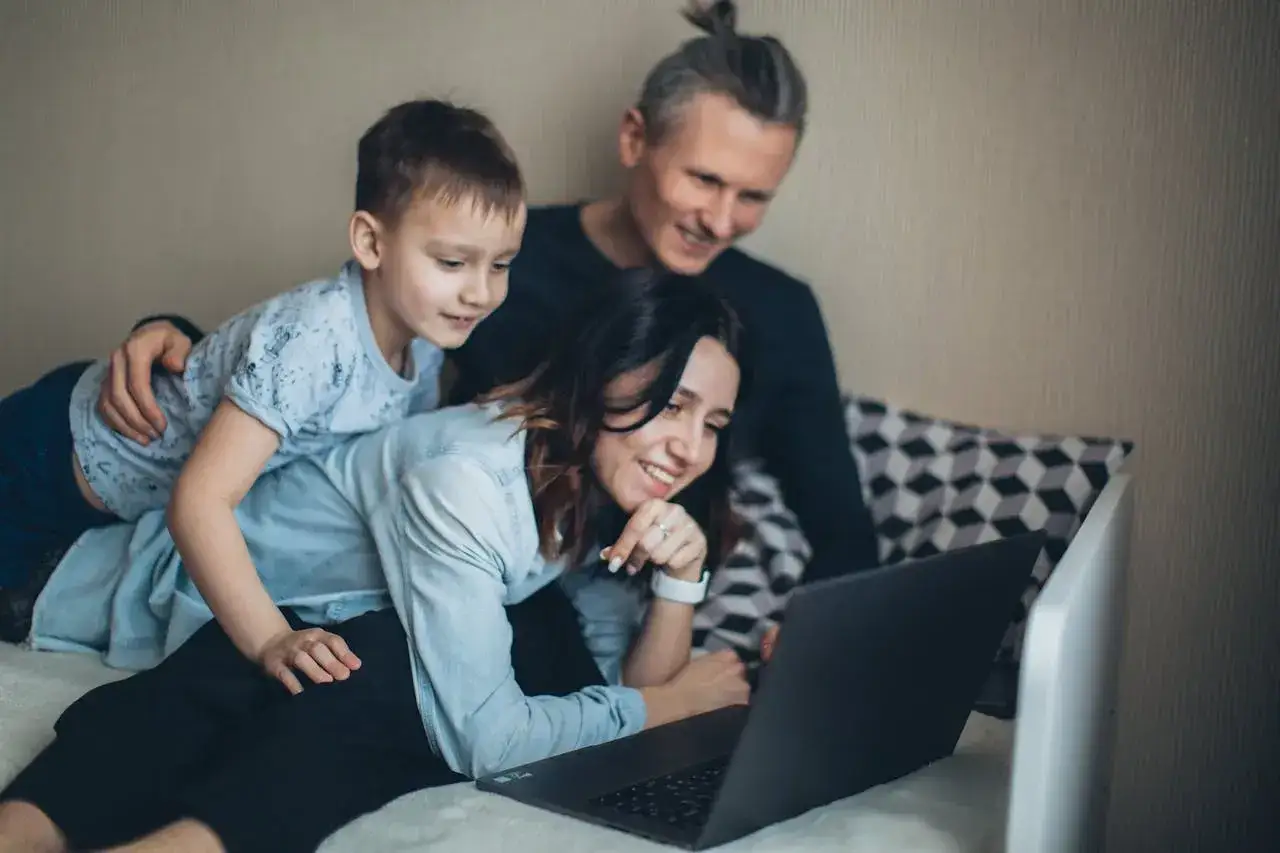 Rodzina ogląda coś na laptopie. Może planują, jak wykorzystać darowiznę 100 tysięcy od rodziców na wspólne wakacje.