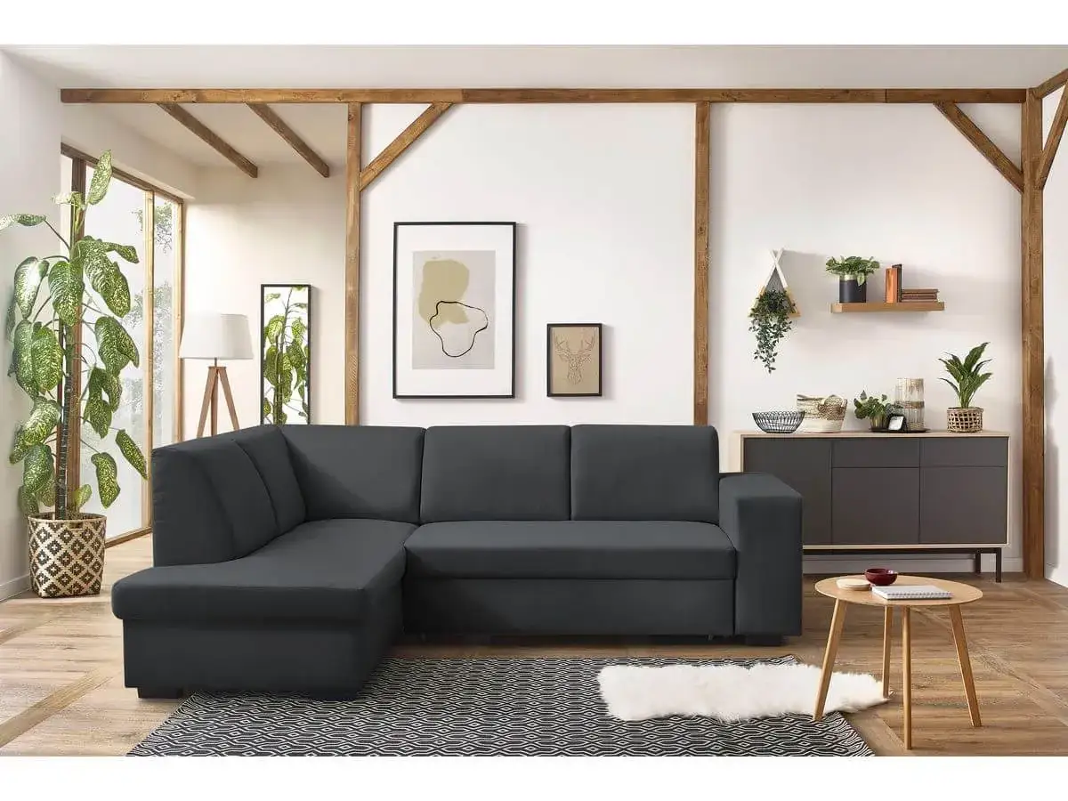 Canapé d'angle gris foncé, parfait pour un salon feng shui. Il est complété par des plantes vertes, des cadres et un meuble bas.