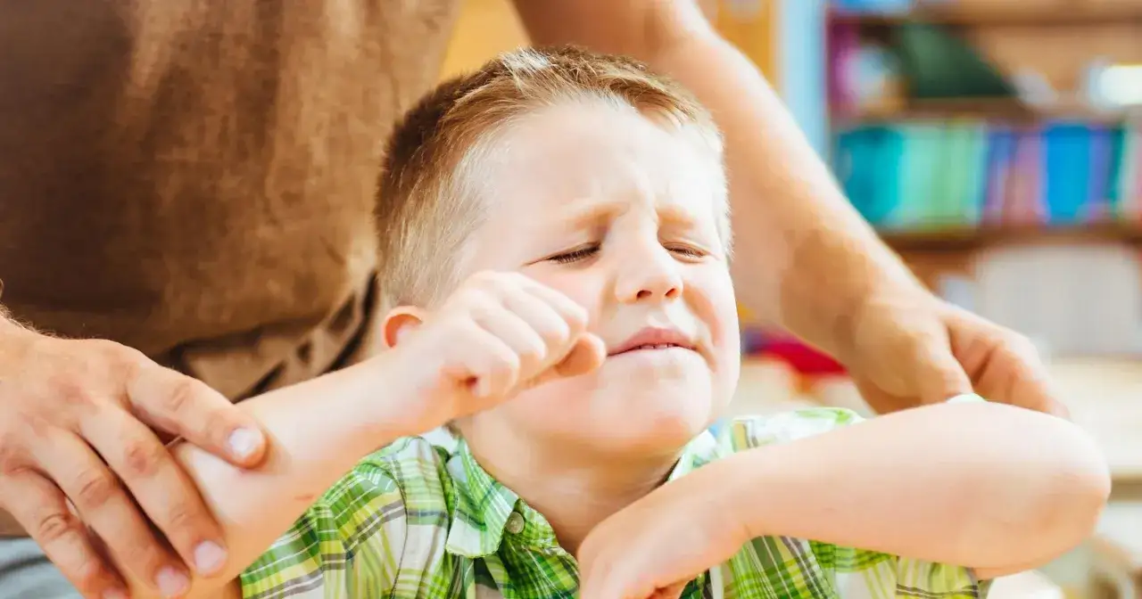 Chłopiec z ADHD, zaciśnięta pięść, zamyka oczy, wyrażając frustrację. Dorosły próbuje go uspokoić.