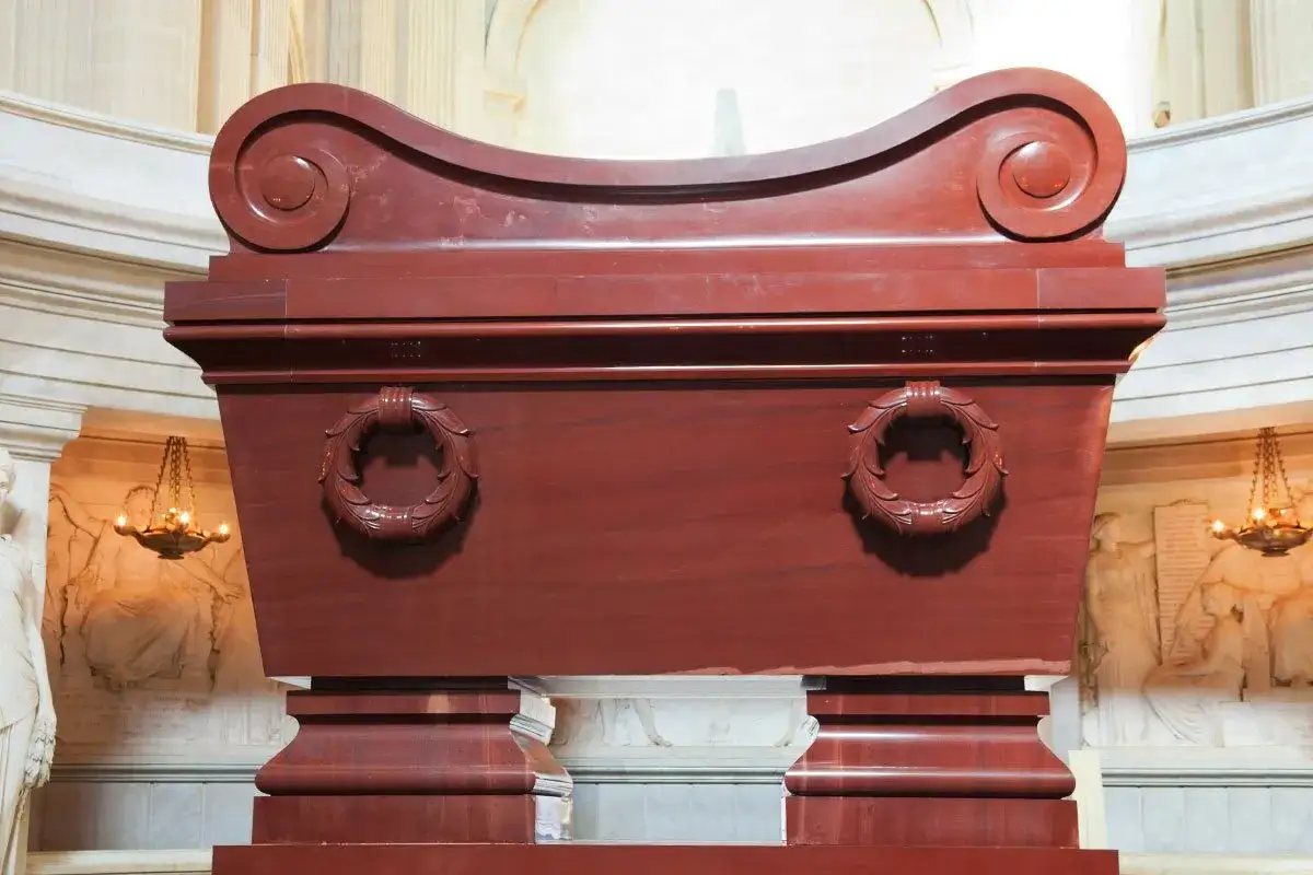 Imponujący, czerwony sarkofag Napoleona z ozdobnymi wieńcami. Monumentalny grobowiec w paryskim kościele Inwalidów.