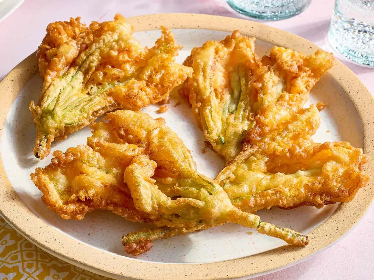 Friterad zucchiniblomma, gyllene och krispiga, ligger på en tallrik. En delikatess som smälter i munnen.