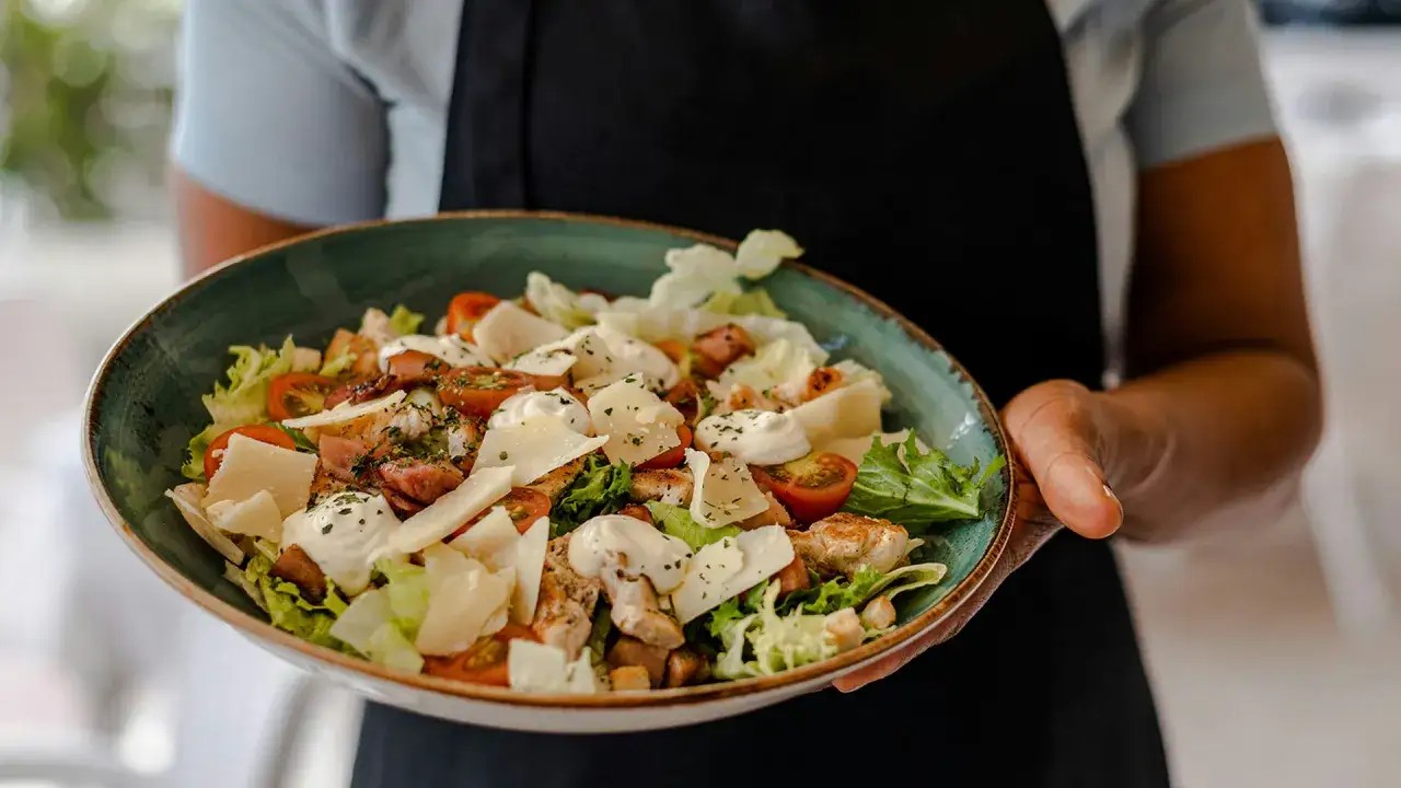 Una generosa ensalada C&eacute;sar con pollo a la parrilla, tomates cherry, queso parmesano y aderezo cremoso, lista para servir.