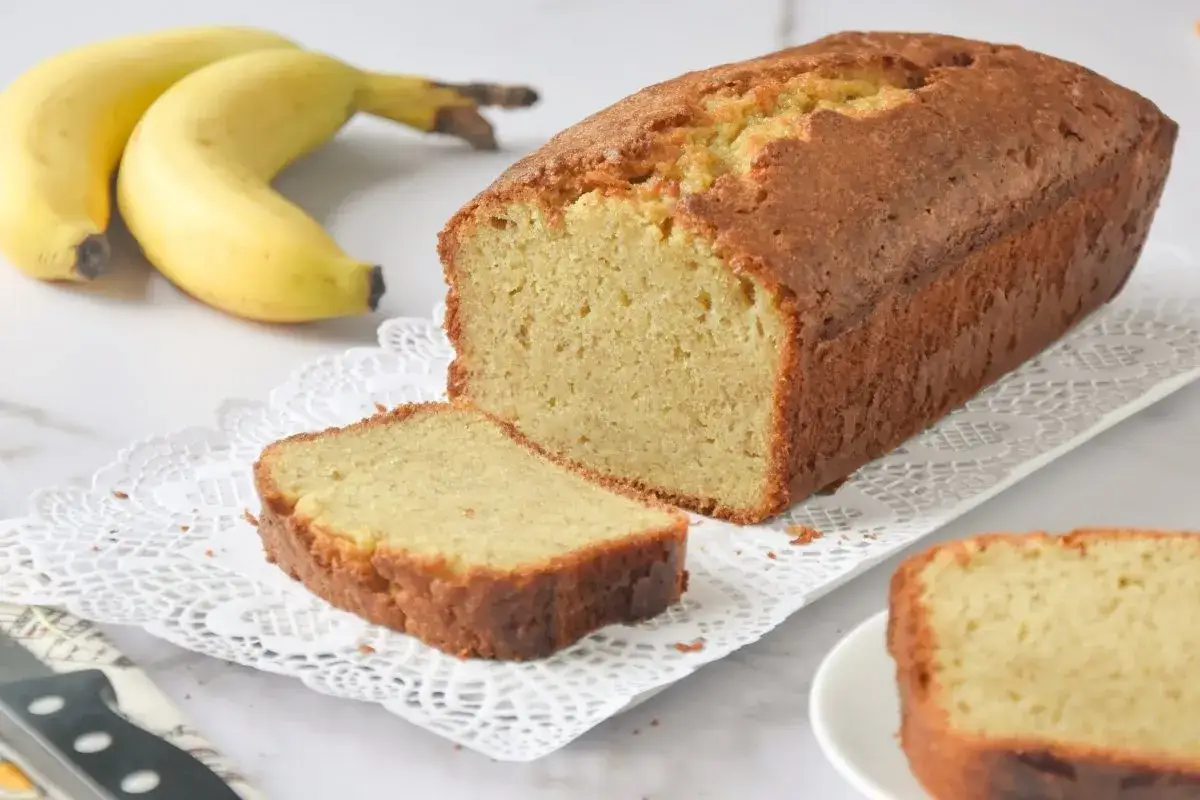 Un delicioso bizcocho de plátano recién horneado, con una rebanada cortada y dos plátanos amarillos al fondo.