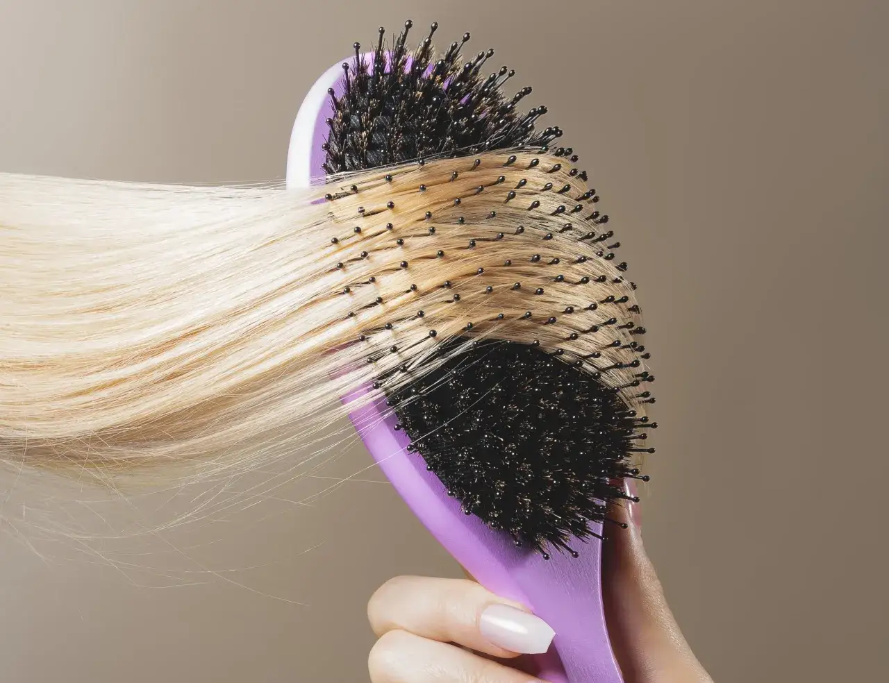 En hand håller en lila borste som borstar blont hår. Håret ser lite torrt ut, kanske med torra toppar.
