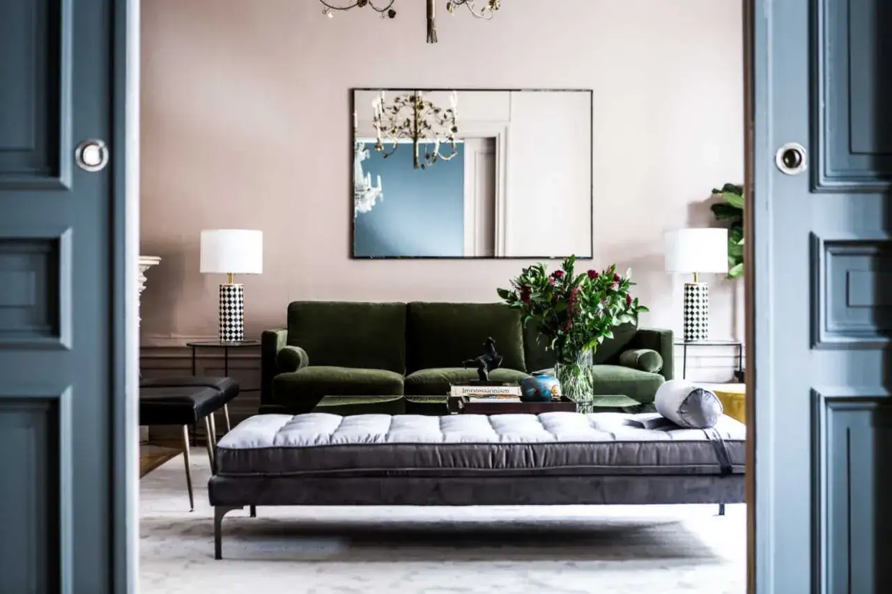 En elegant soffgrupp i art deco-stil, med en gr&ouml;n sammetssoffa och en gr&aring; ottoman, som p&aring;minner om lyxiga hem i Stockholm.