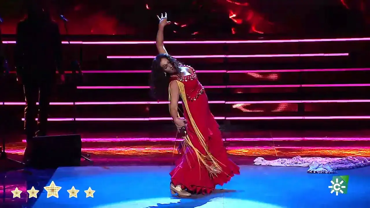 Susana Casas, bailaora, deslumbra con un vestido rojo vibrante y movimientos apasionados en un escenario iluminado.