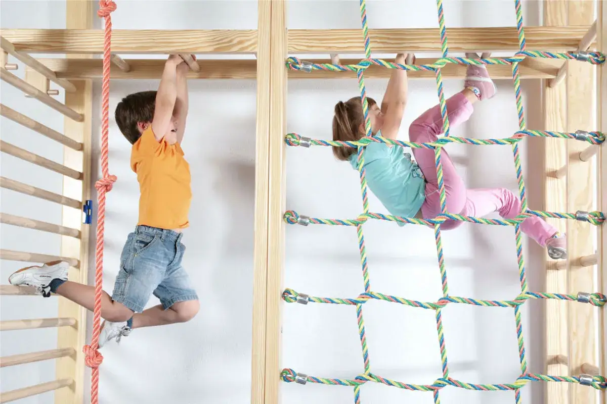 Kinder klettern und schwingen an einer bunten Seilnetz-Bewegungslandschaft im Kindergarten.