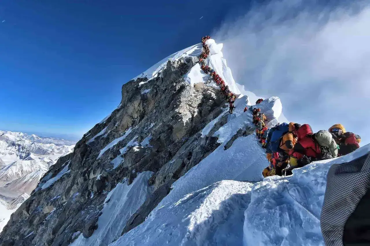 Kolejka **szerpów** i alpinistów na zboczu góry, wspinających się w trudnych warunkach.