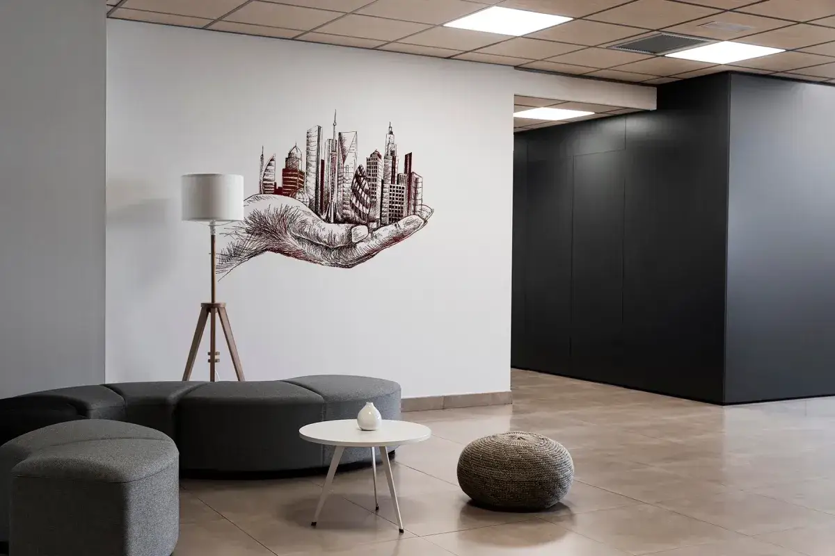 Wnętrze z nowoczesnymi meblami i grafiką na ścianie przedstawiającą dłoń trzymającą panoramę miasta. To idealne miejsce na wydruk zdjęć duży format.