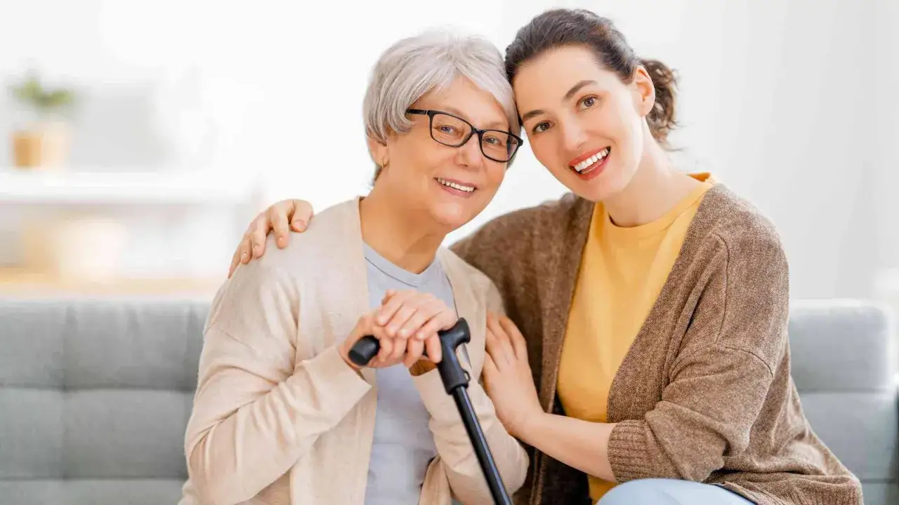 Due donne sorridono, una anziana con bastone e occhiali, l'altra più giovane. Un'immagine che evoca cura e supporto, come per il modello ap70 indennità di accompagnamento.