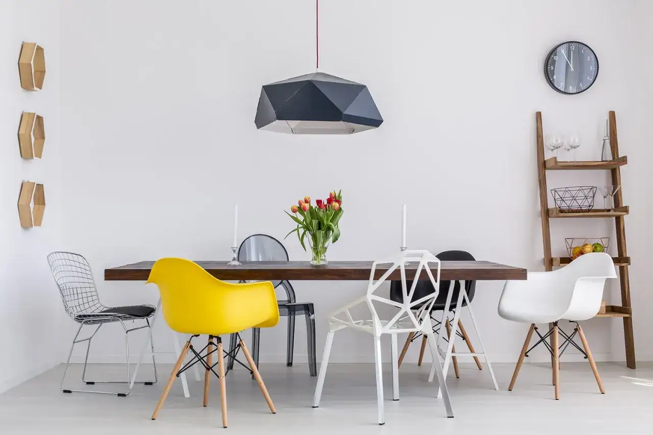 Un tavolo da pranzo con sedie di design in vari colori e forme. Un giallo vivace, un bianco geometrico e un grigio trasparente creano un mix eclettico per abbinare sedie al tavolo.