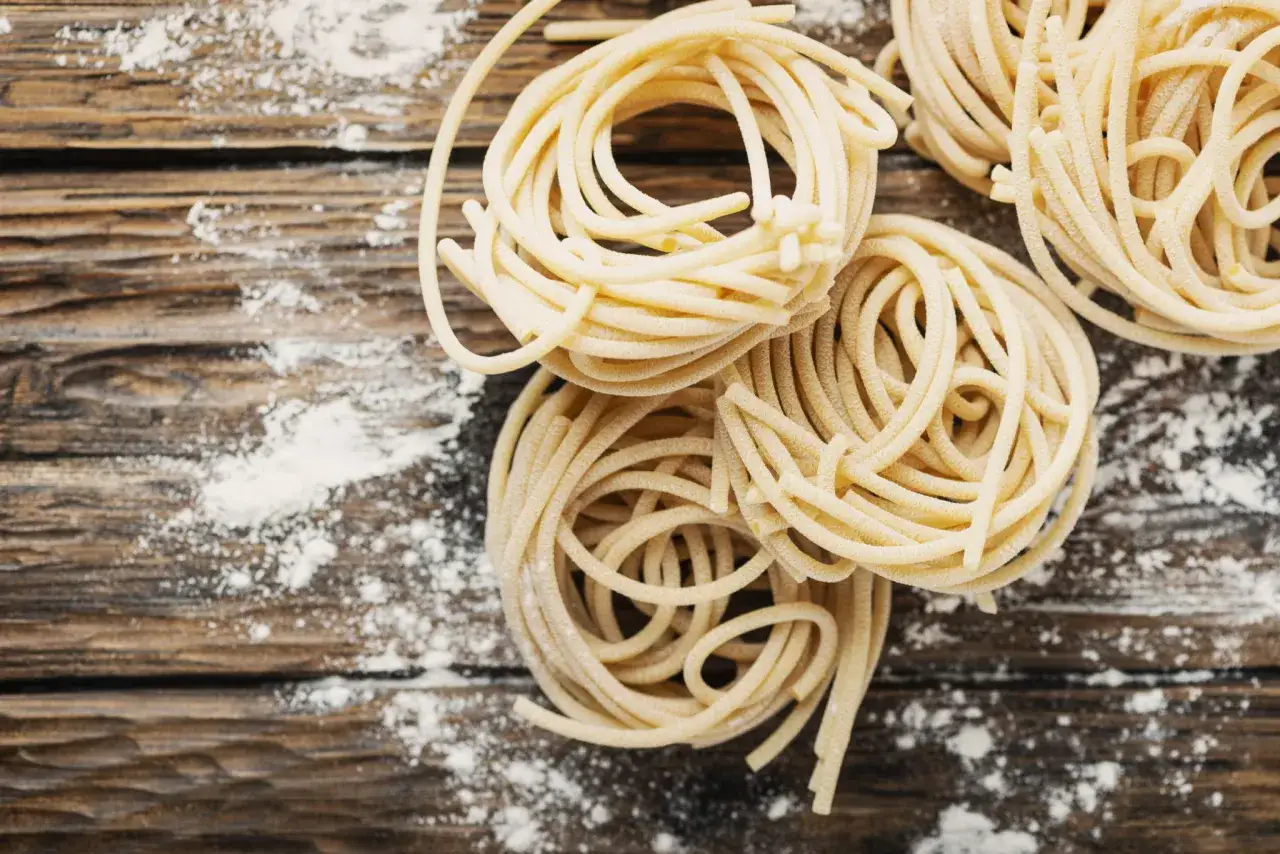 Nidi di pici toscani freschi, spolverati di farina su un tagliere di legno grezzo.