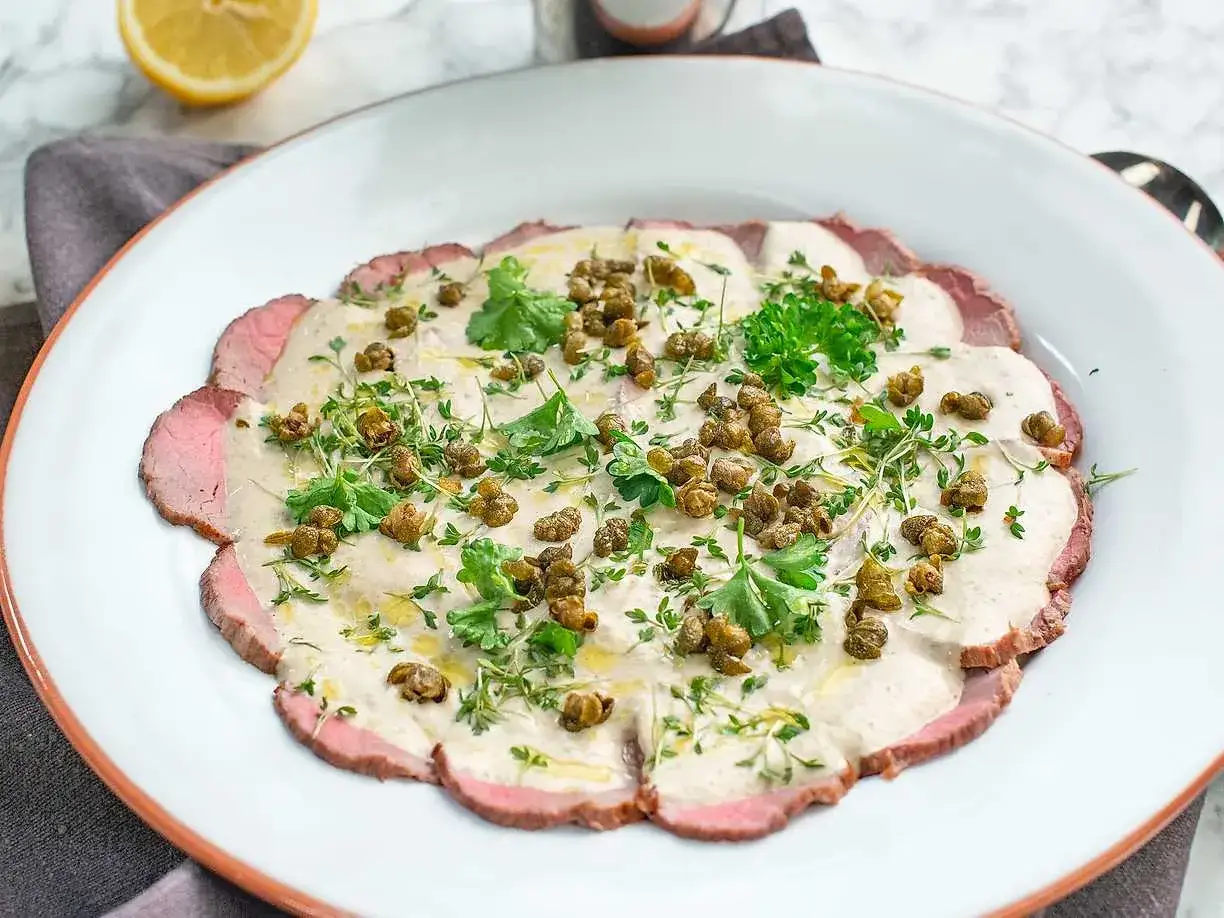 En vacker tallrik med tunt skivad kalvfilé, täckt av en krämig tonfisksås, kapris och färska örter. Ett perfekt vitello tonnato recept för en festlig måltid.