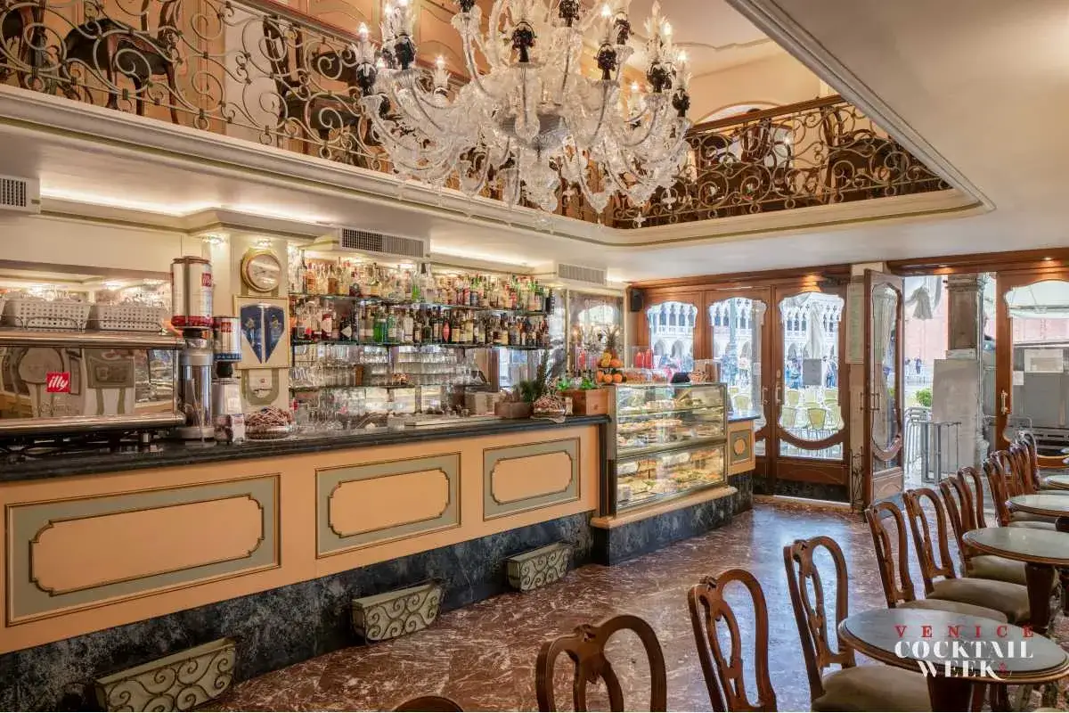 Interno di un caffè storico a Venezia, con bancone bar, vetrine di dolci e un lampadario di cristallo.