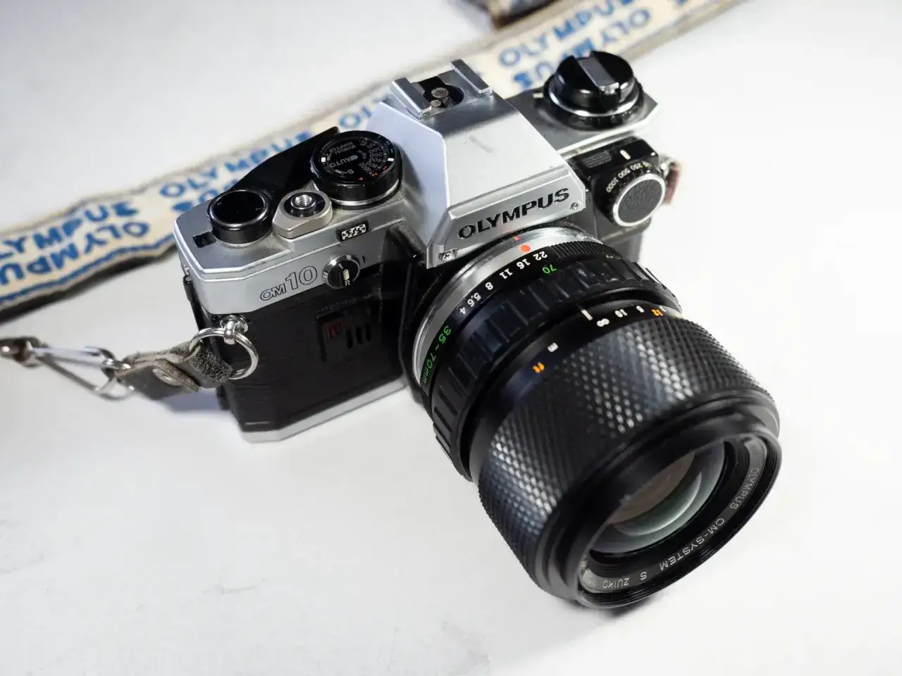 En klassisk Olympus OM-10 systemkamera med objektiv och en Olympus-rem. Perfekt f&ouml;r att f&aring;nga minnen.