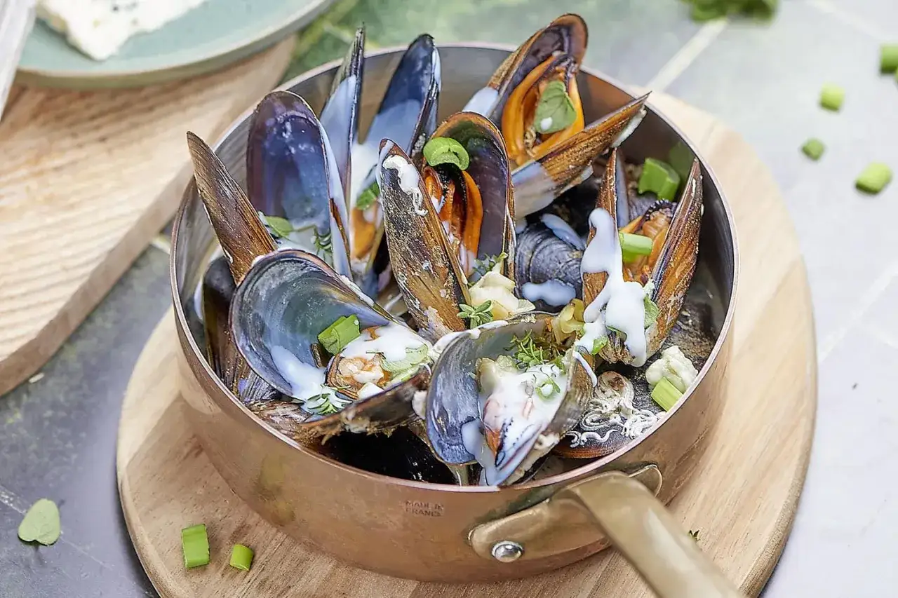 D&eacute;licieuses moules au roquefort dans une casserole en cuivre, napp&eacute;es d'une sauce cr&eacute;meuse et garnies de ciboule. Un plat savoureux &agrave; d&eacute;guster.
