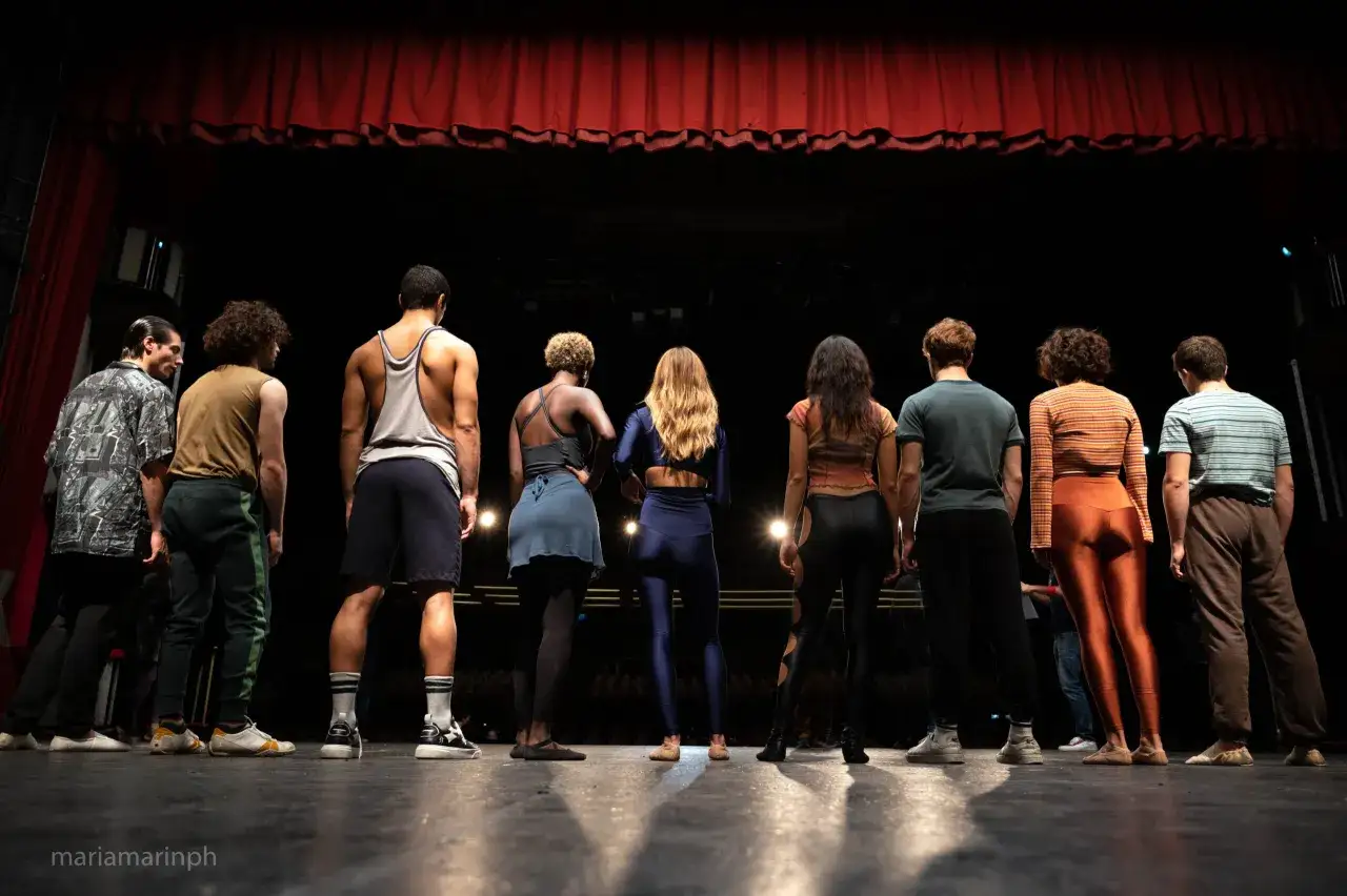 Un gruppo di giovani attori attende sul palco, le luci soffuse creano ombre lunghe. Sono pronti per le musical it audizioni.
