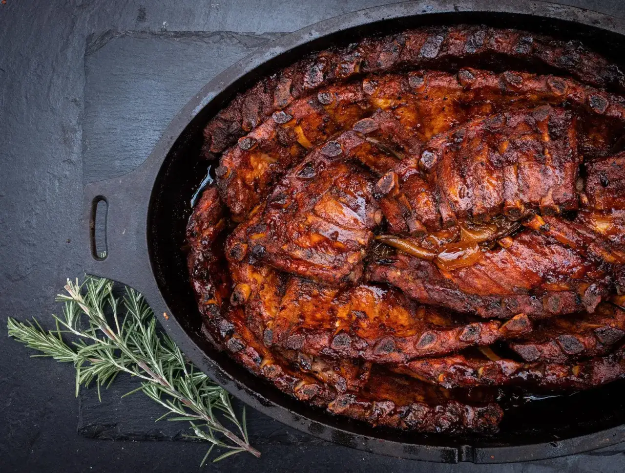Saftige spareribs im Dutch Oven, glasiert und bereit zum Genie&szlig;en. Ein Rosmarinzweig liegt daneben.