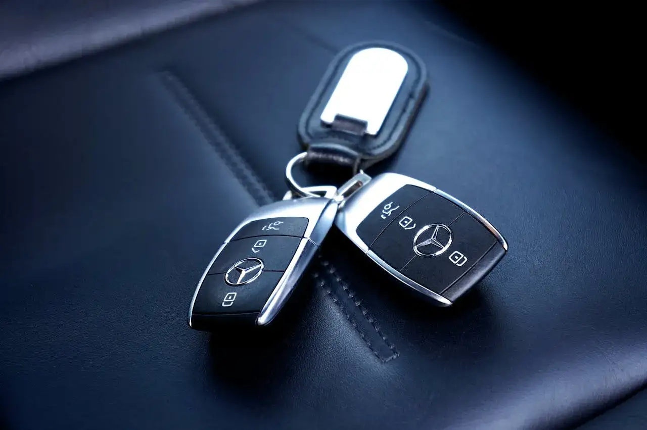 Dwa kluczyki samochodowe Mercedes na czarnej, skórzanej tapicerce. Zastanawiasz się, ile kosztuje dorobienie klucza do samochodu z immobilizerem?