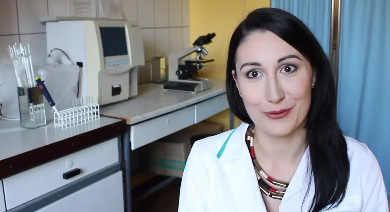 Uśmiechnięta diagnosta laboratoryjna w białym fartuchu, obok mikroskopu i aparatury medycznej.