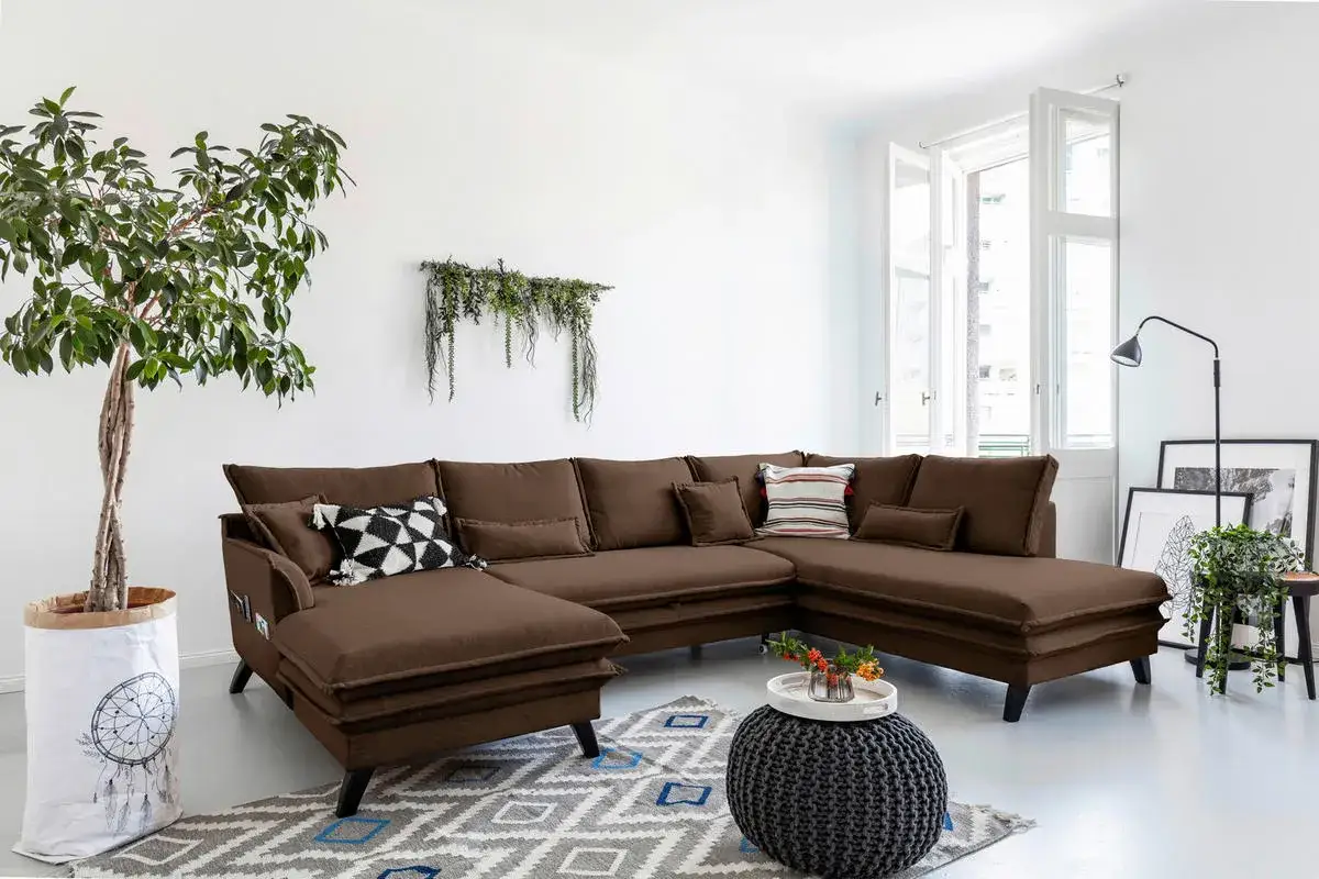 En rymlig, brun soffa med många kuddar. En stor grön växt står bredvid.