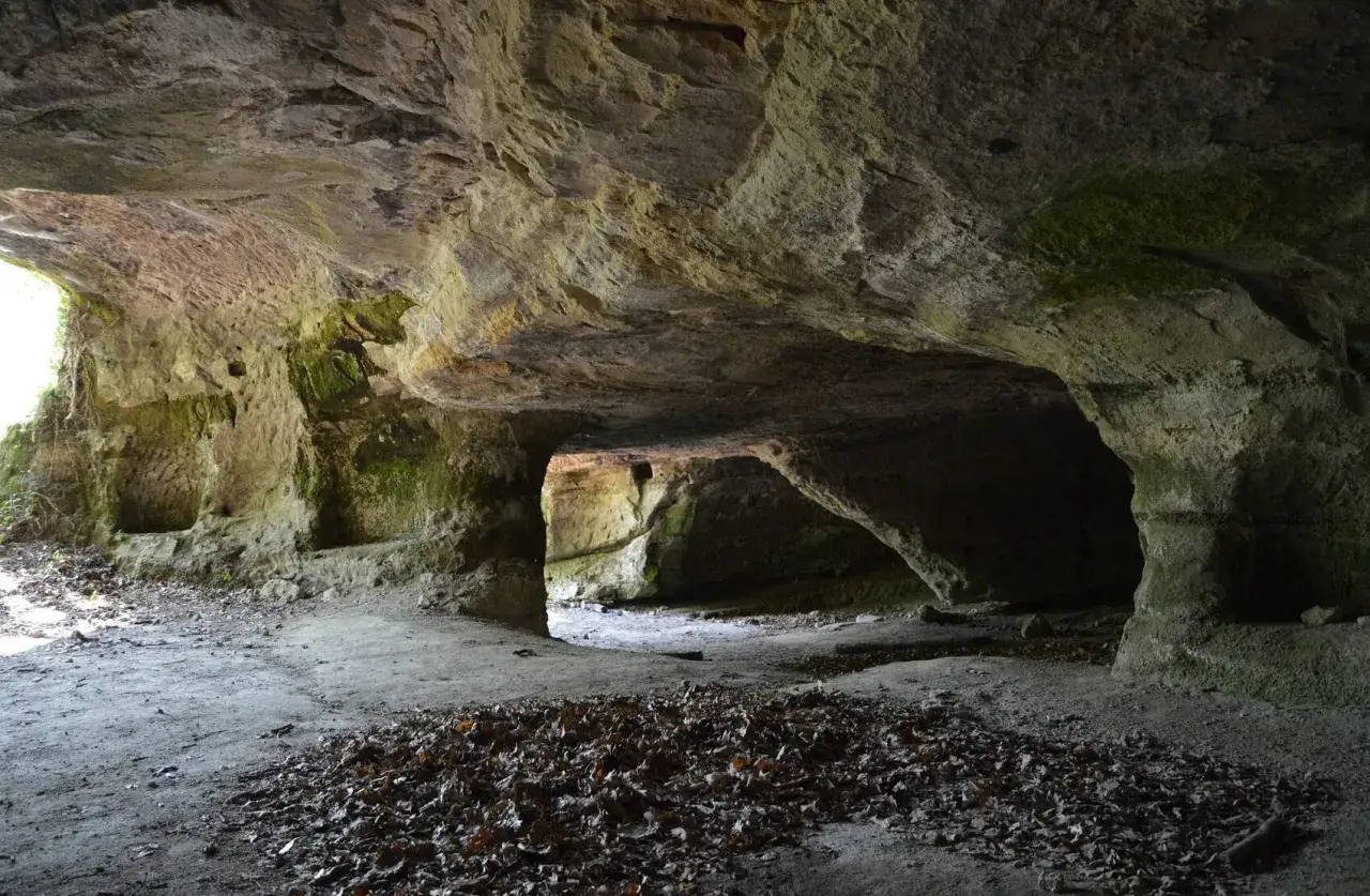 L'interno di una grotta scavata nella roccia, con nicchie e passaggi che evocano Vitozza, la città perduta.