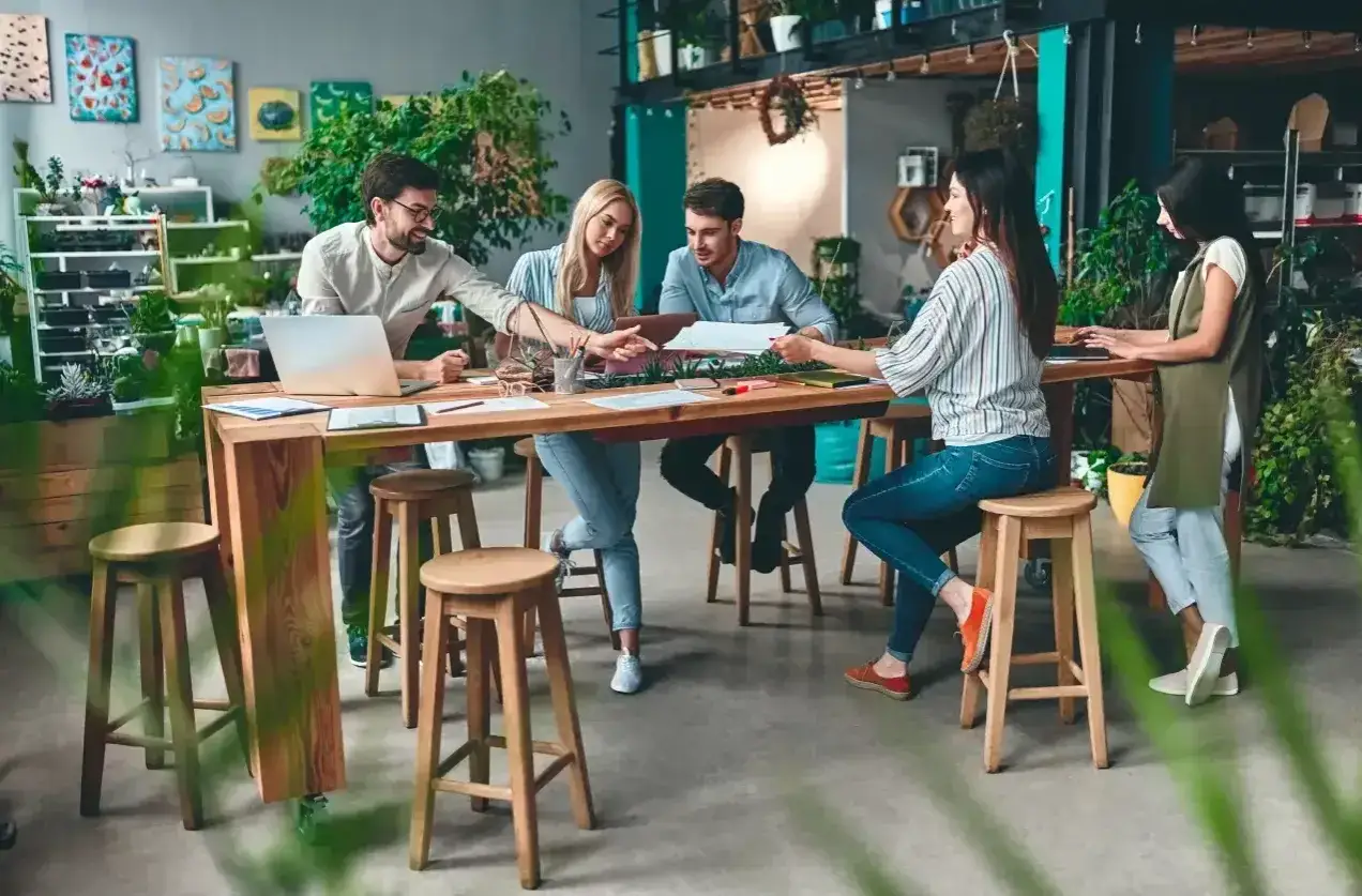 Ett team diskuterar vid ett bord i en grönskande miljö, vilket visar på flexibla arbetsformer.