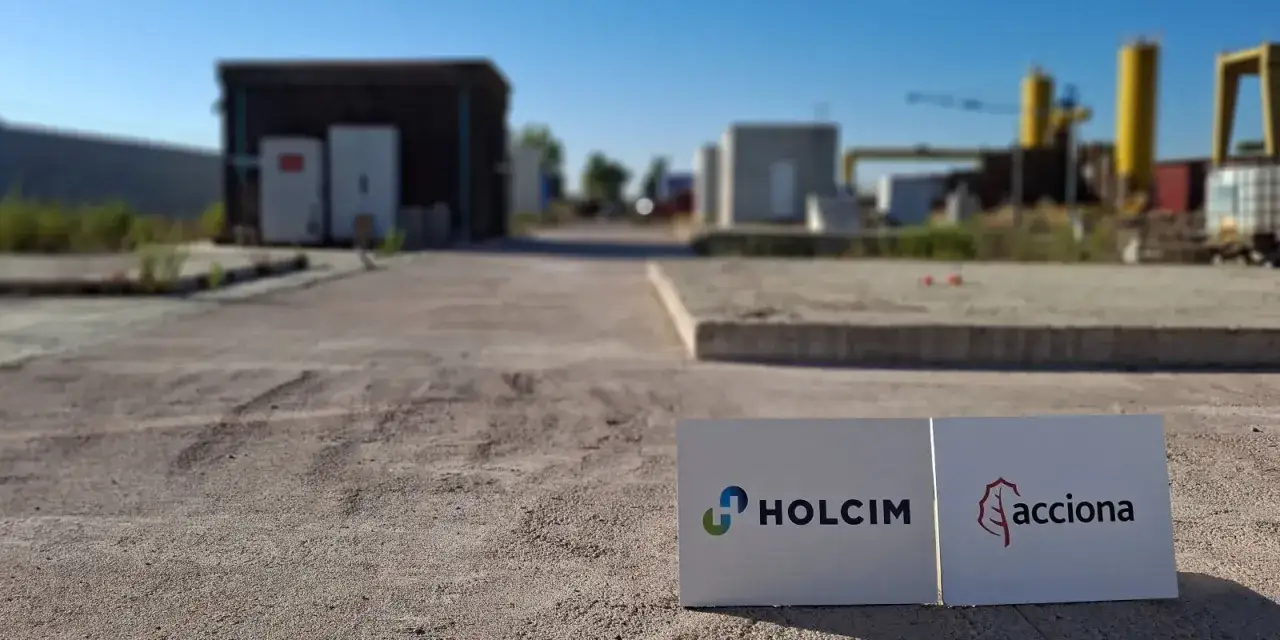 Dos carteles con los logos de Holcim y Acciona, empresas del MBCC Group, en un &aacute;rea industrial.