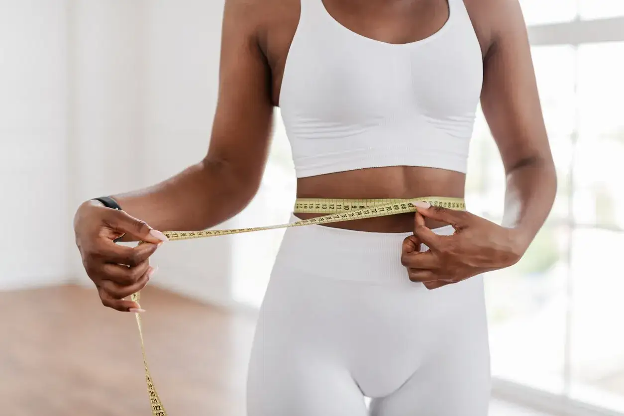 Femme mesurant sa taille avec un mètre ruban, un signe de progrès pour comment affiner sa taille.