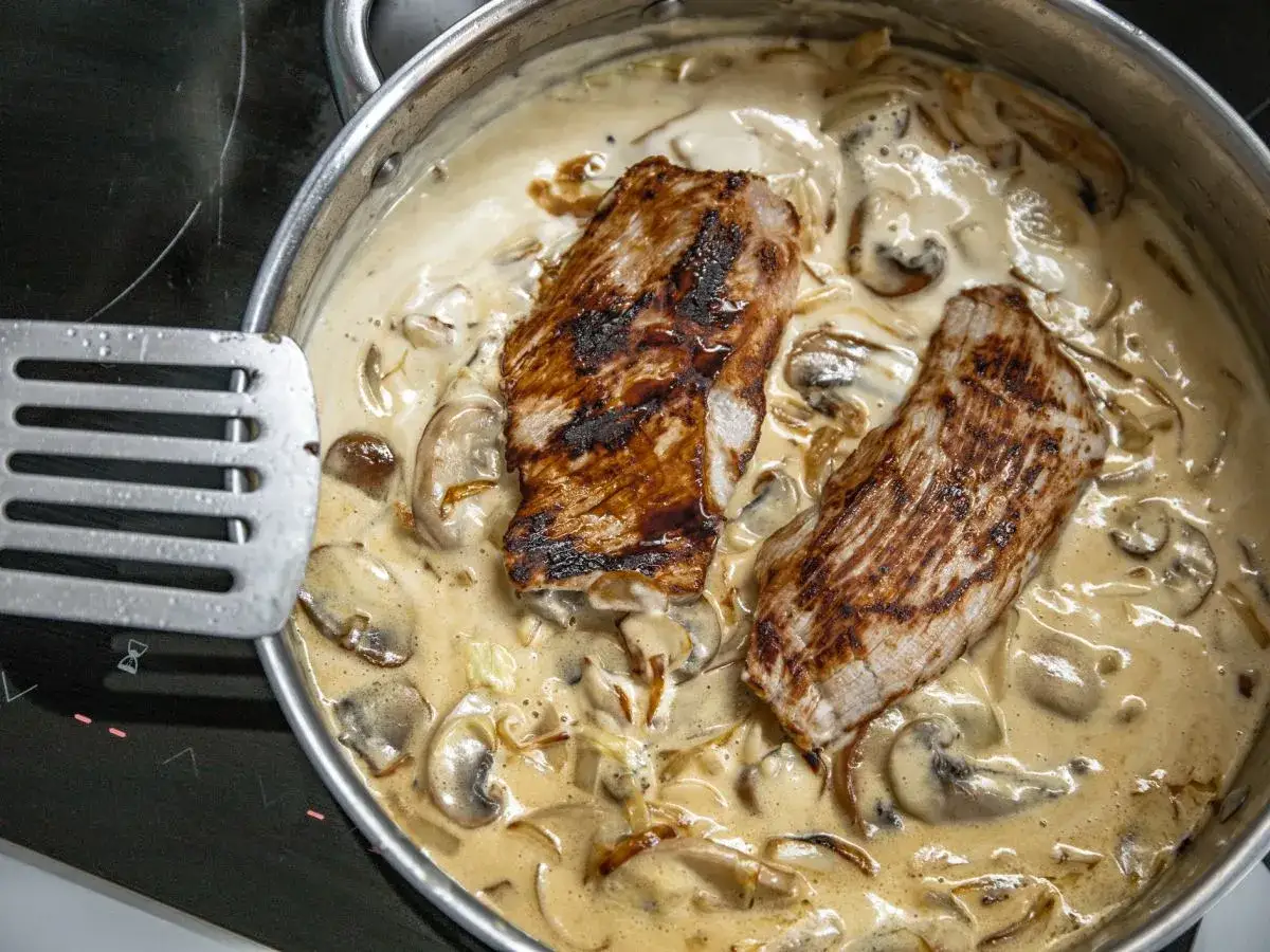 Dwa kawałki grillowanego mięsa w kremowym sosie pieczarkowym. Idealny przepis na to, jak zrobić sos pieczarkowy z pieczarek.