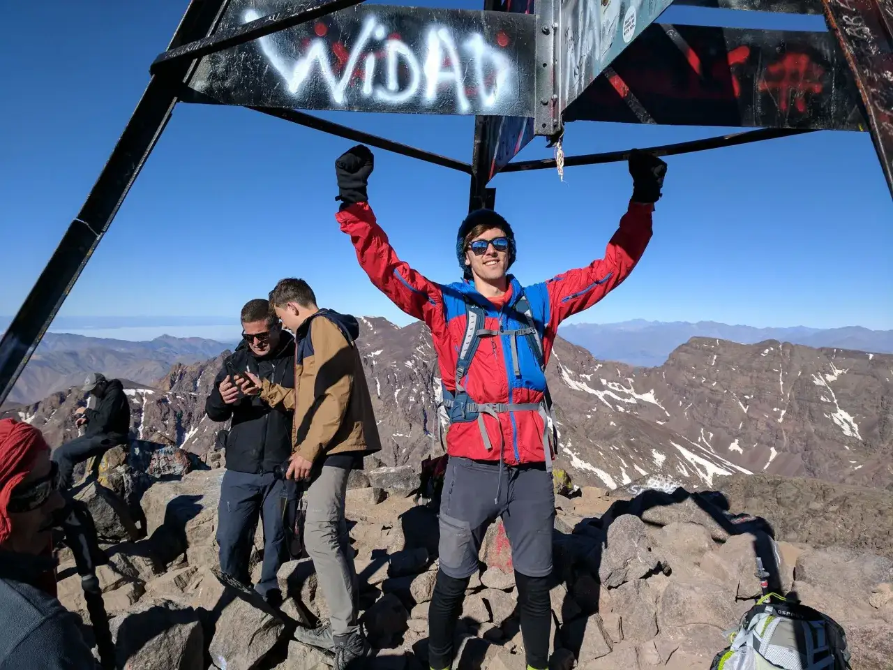 Szczyt Jabal Toubkal zdobyty! Radosny turysta z rękami w górze na tle górskiego krajobrazu.