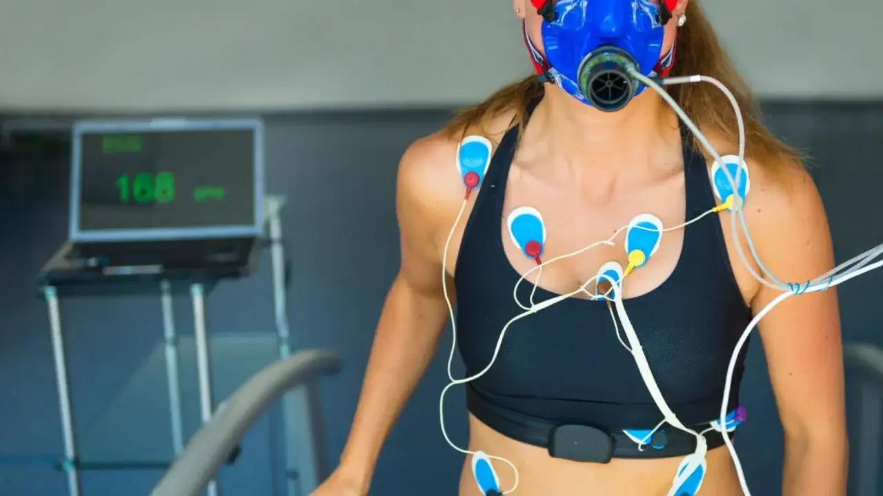 Femme portant un masque et des &eacute;lectrodes pour un test d'effort cardiologue. L'&eacute;cran affiche 168 bpm.