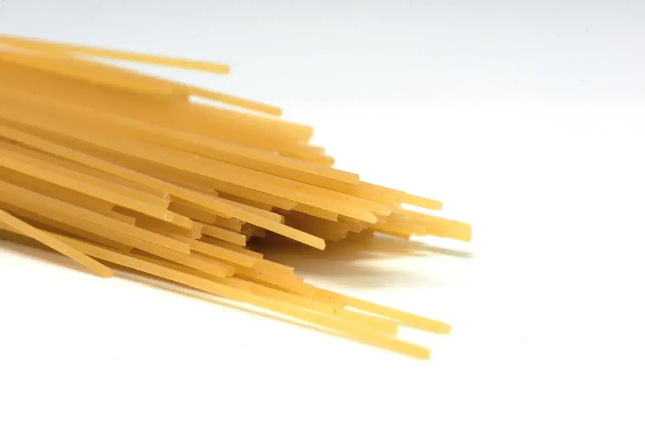 Pęczek żółtego makaronu spaghetti na białym tle. Zastanawiasz się, ile cm ma makaron spaghetti? Zazwyczaj około 25-30 cm.