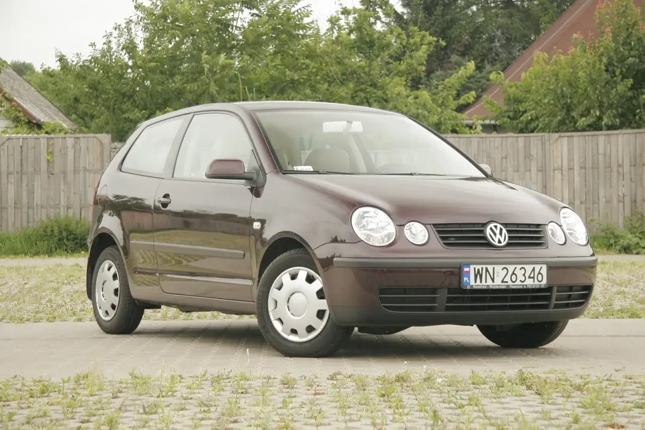 Ciemnobordowy Volkswagen Polo 9N, z widocznym wykazem żarówek w reflektorach, zaparkowany na kostce brukowej.