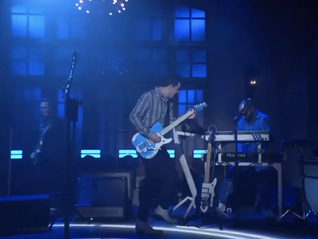 Jack White gra na niebieskiej gitarze na scenie z niebieskim oświetleniem.