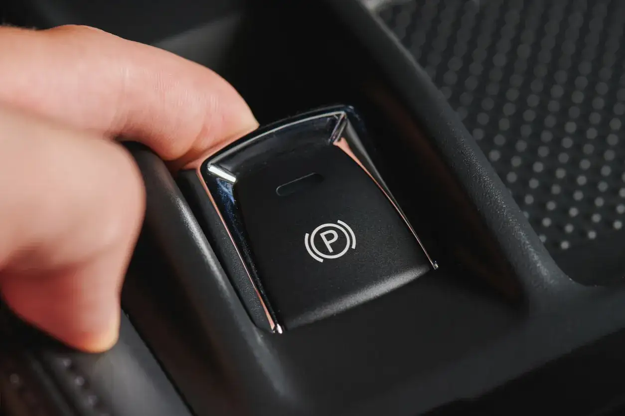 Main d'une personne appuyant sur le bouton du frein à main automatique pour le débloquer.