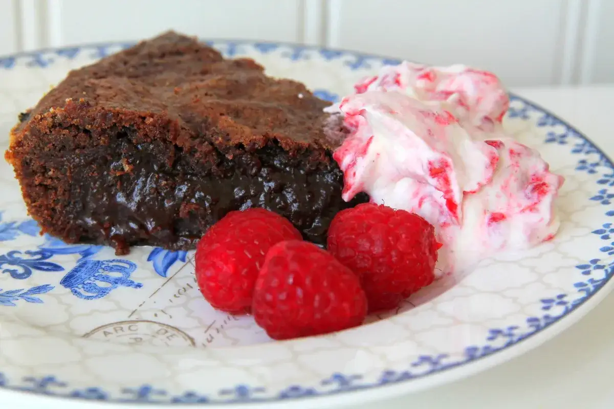 En bit kladdkaka med lakrits, serverad med vispad grädde och hallon.