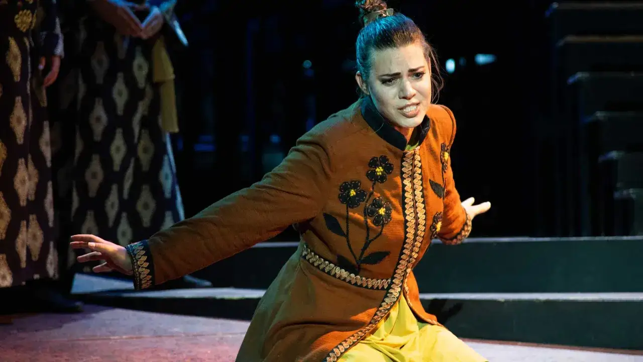 En skådespelerska i en broderad brun jacka, med en dramatisk min, under en föreställning av operan Turandot.