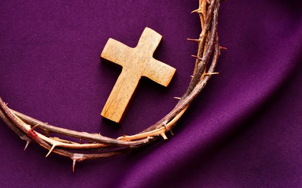 Couronne d'&eacute;pines et croix en bois sur un tissu violet, &eacute;voquant la couleur spirituelle du sacrifice et de la p&eacute;nitence.