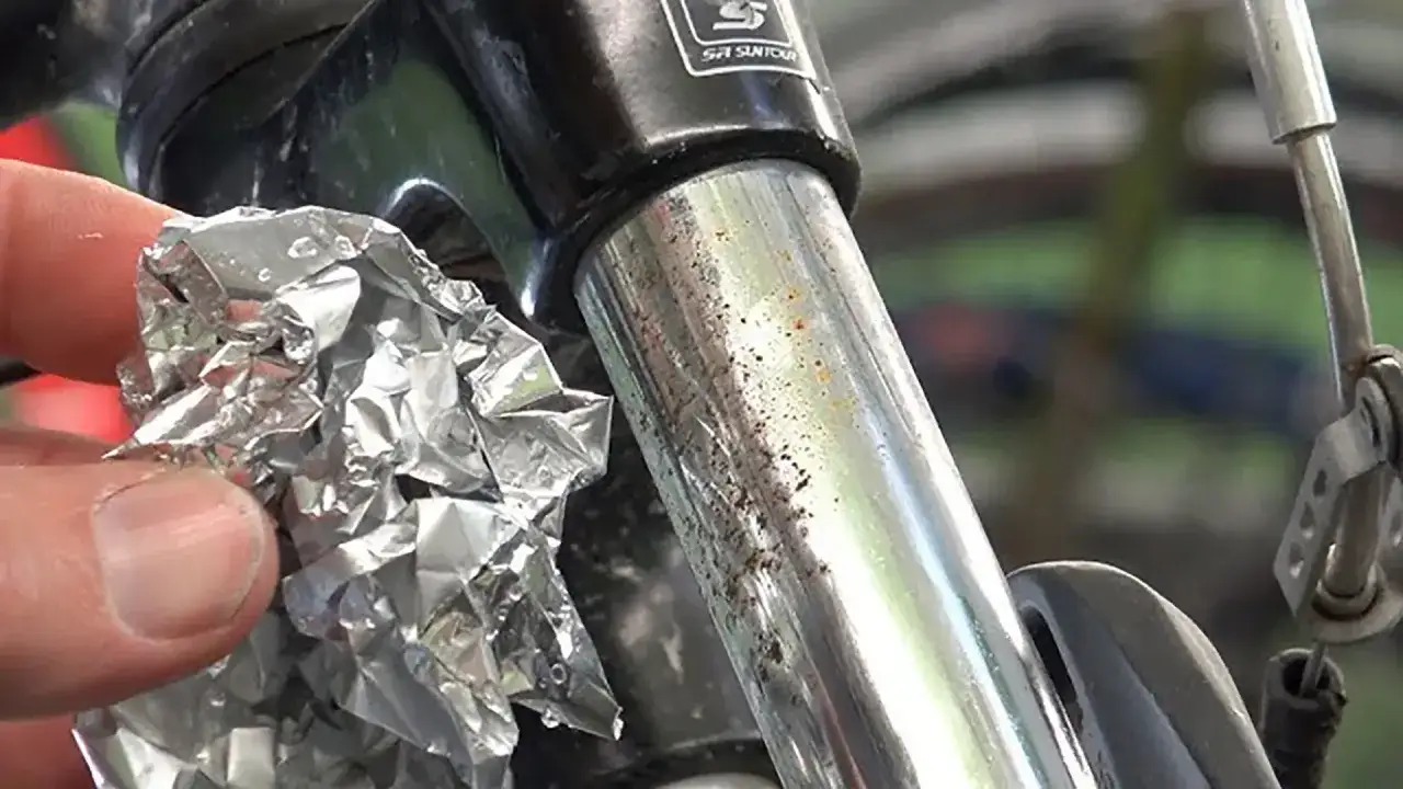 Mano con foglio d'alluminio vicino a stelo forcella bicicletta con macchie di ruggine e sporco.