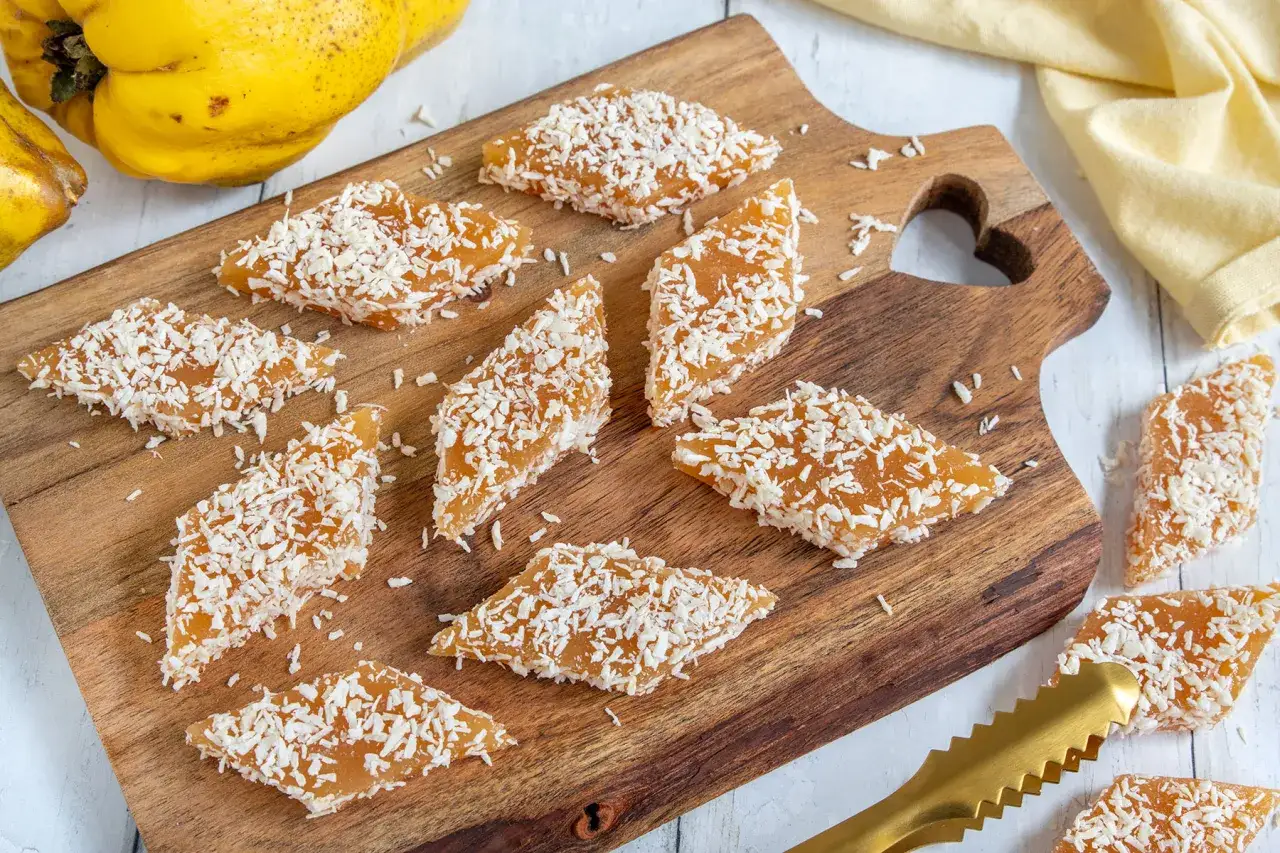 Quittenbrot-St&uuml;cke mit Kokosraspeln bestreut auf einem Holzbrett. Ein einfaches Rezept f&uuml;r Quittenbrot.