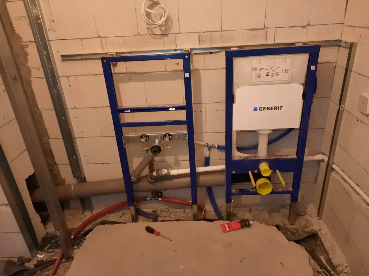 Montaż stelaża Geberit, przygotowanie do podłączenia geberitu do odpływu. Widoczne rury i elementy instalacji wodno-kanalizacyjnej.