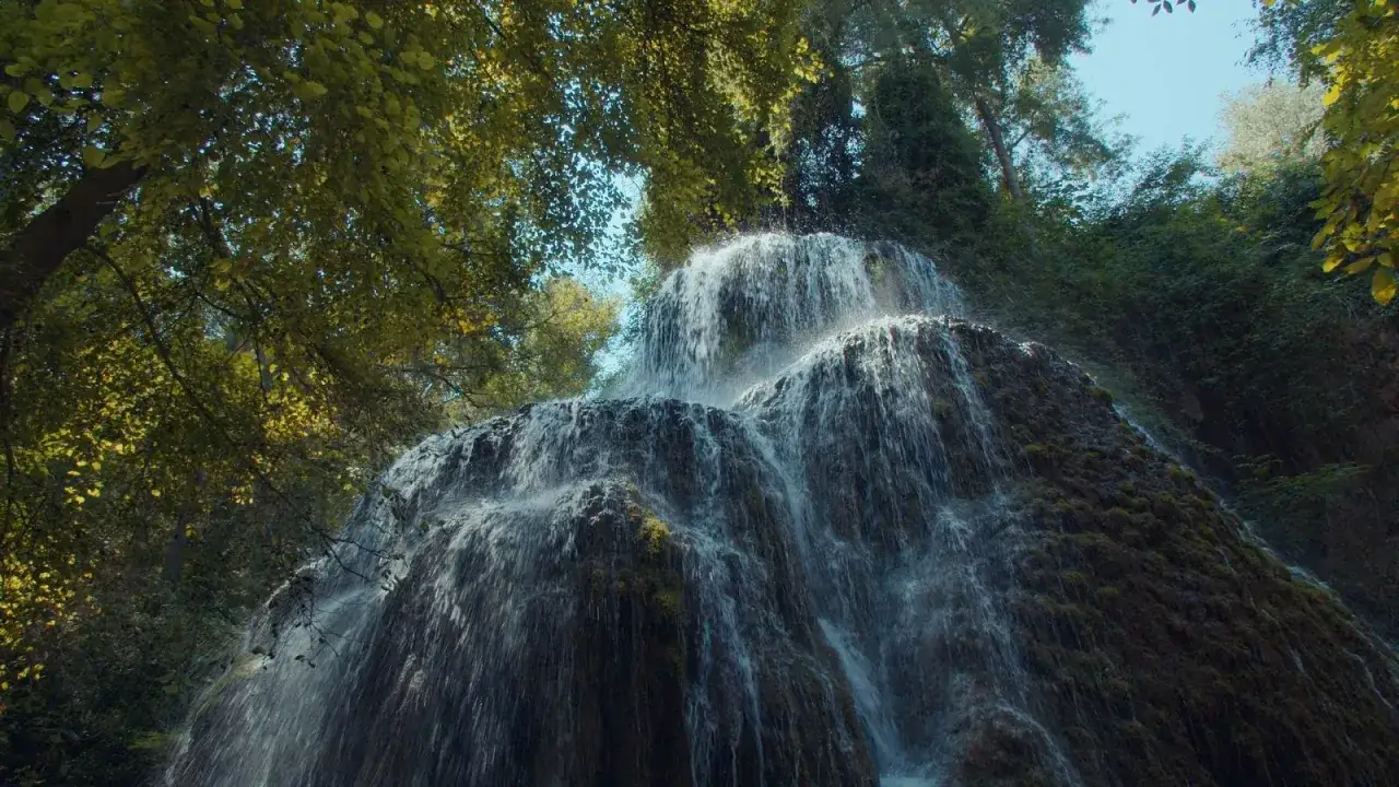 Cascada exuberante, escenario natural donde se rodó Traitors España. El agua cae en cascada sobre rocas cubiertas de musgo, rodeada de árboles frondosos.