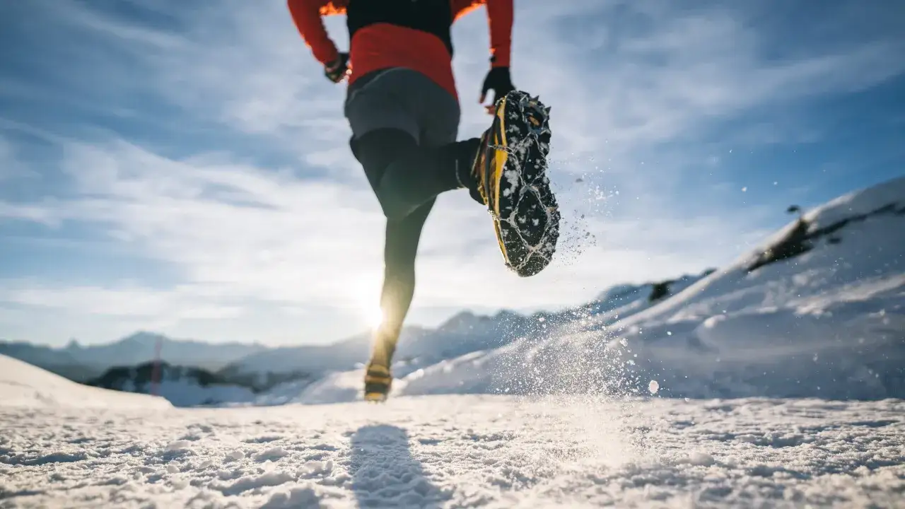 L&auml;ufer mit Spikeschuhen im Schnee, bereit f&uuml;r Trailrunning Training. Die Sonne scheint hinter den Bergen.